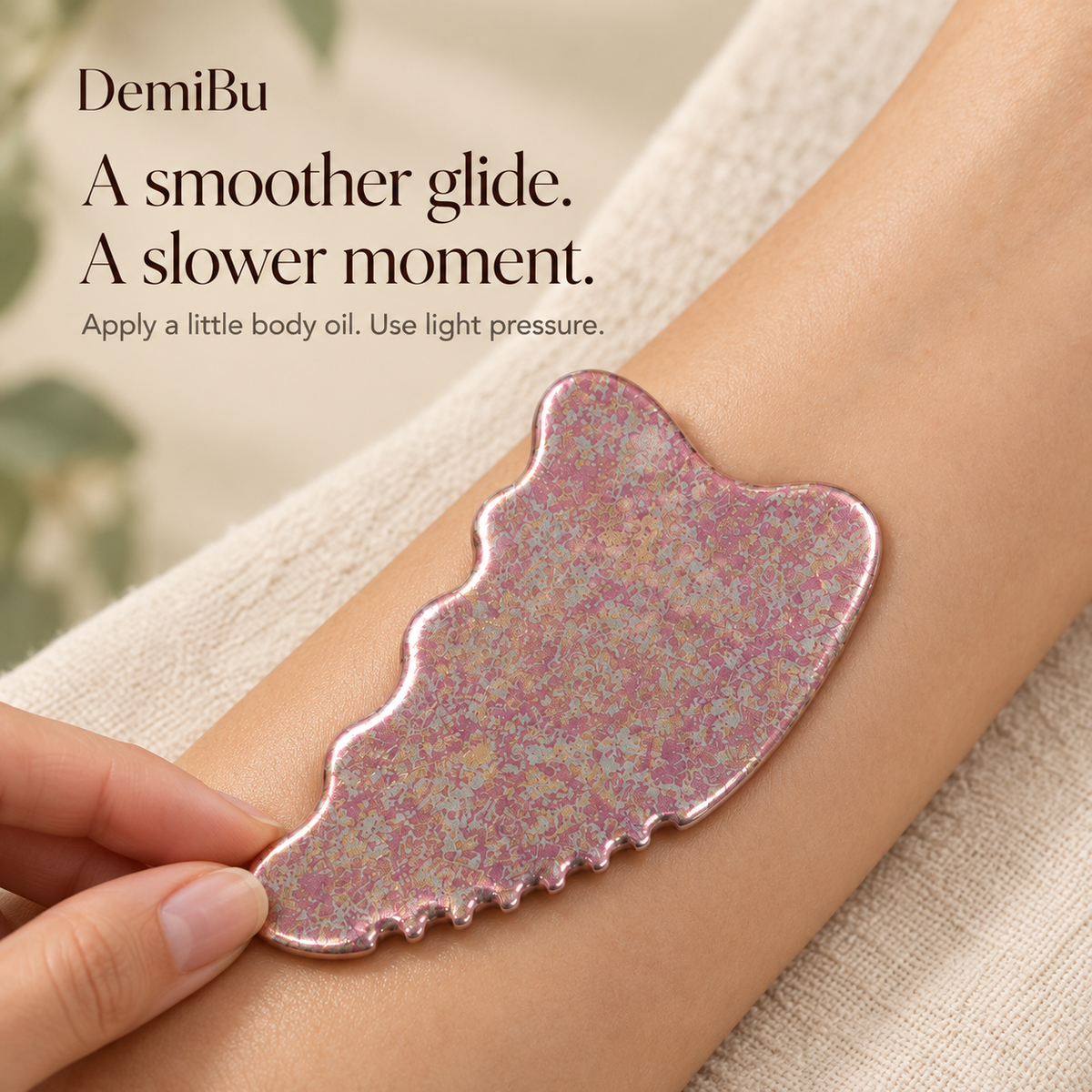 An adult gently gliding the Crystalline Rose titanium gua sha over an oiled forearm during body massage