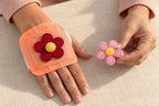 A red flower decoration on a hand warmer, with a pink flower held nearby as another styling option.