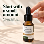 A close view of the black dropper cap and amber-glass DemiBu Mugwort Massage Oil bottle with fingertips beside the collar.