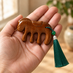 The horse comb held in an open palm, its green silk tassel hanging below.