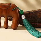 Macro view of the green silk tassel, silver cap and jade-green bead tied to the saddle of the comb.