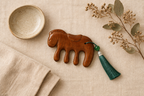 Flat lay of the horse comb on cream linen with a ceramic dish and dried foliage.